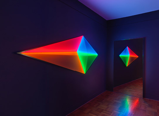 Brightly coloured prism illuminates dark room and is reflected in mirror.
