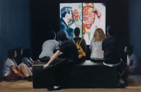 A group of people sit looking at an artwork in a dimly lit room