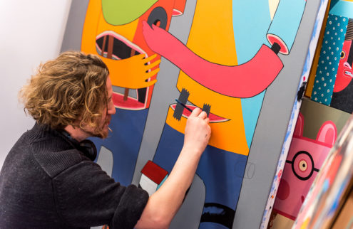 A man paints detail onto a colourful canvas