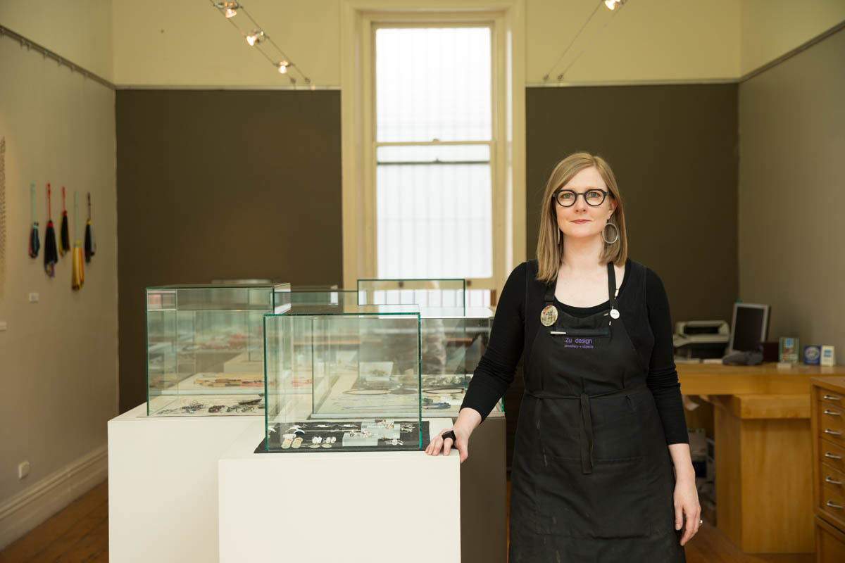 A woman stands next to a glass case which holds a variety of different objects