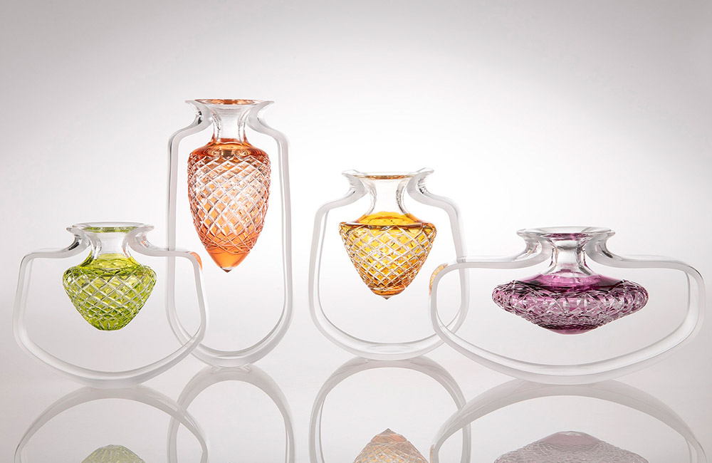 Four glass vessels of varying shapes coloured in the centre lime green, orange, yellow and purple.