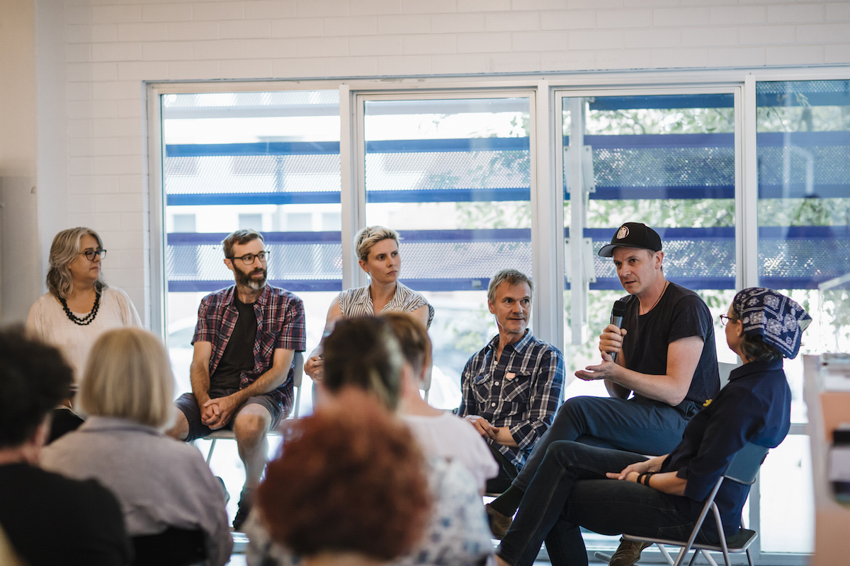 A group of people sit in a circle around a conference room and listen to an individual speaker