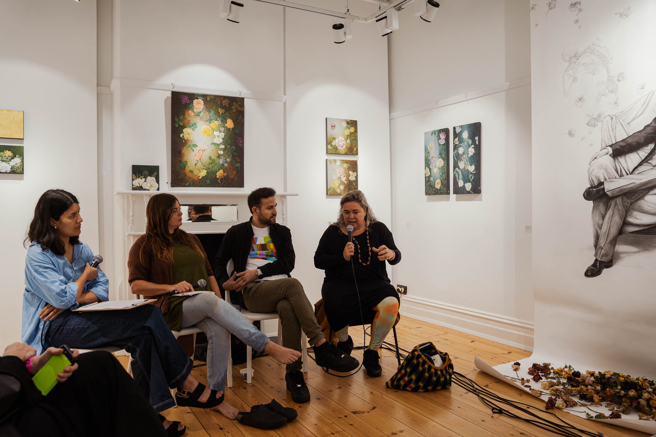 Three people stand in front of a desk and a wall of artwork, looking directly into the camera