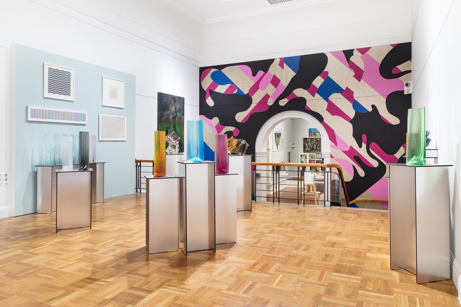 Three people stand in front of a desk and a wall of artwork, looking directly into the camera